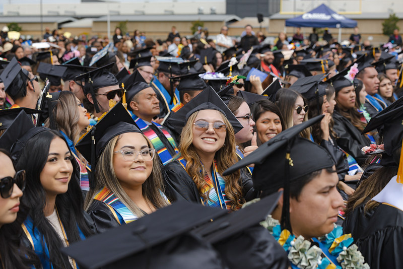 A crowd of students sitting and wearing graduation caps and gowns. 